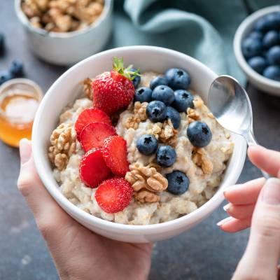 Oatmeal porridge bowl with berry fruits in female hands Oatmeal porridge bowl with berry fruits in female hands, closeup view. Healthy vegetarian breakfast food